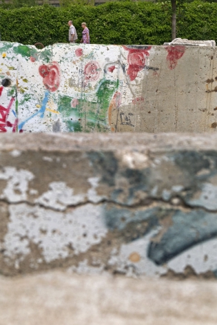  Un couple passe derrière des pièces originales du mur. Ces morceaux de mur sont intégrés à la sculpture ‟Balance‟ de l'artiste Stephan Balkenhol sur le parvis de l'Axel Springer. Berlin, juillet 2009. 
